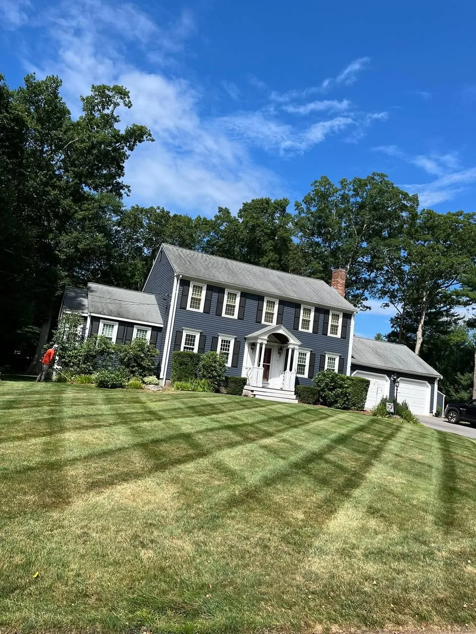 Striped, freshly mowed front lawn at a navy colonial home on a clear summer day.